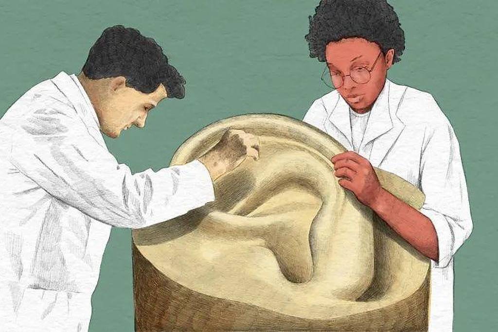 A imagem mostra duas pessoas em um ambiente de trabalho, ambas vestindo jalecos brancos. Um homem está esculpindo uma grande escultura de um ouvido, enquanto uma mulher observa atentamente, segurando a escultura. O fundo é de uma cor verde sólida, destacando a cena. A escultura é feita de um material que parece ser pedra ou argila.