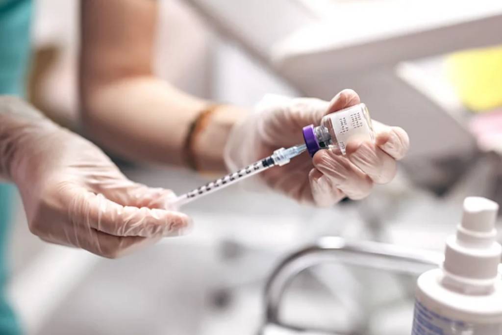 Foto mostra mãos de uma profissional de saúde branca manuseando ampola e seringa para aplicar botox.