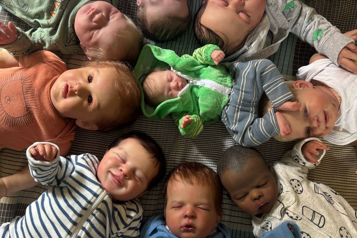A imagem mostra um grupo de bonecos de bebê do tipo reborn dispostos em círculo sobre uma superfície. Os bonecos têm diferentes características, como cores de pele e roupas variadas, incluindo pijamas e macacões. Eles estão com expressões faciais que imitam bebês reais, e a disposição cria uma composição visual interessante.
