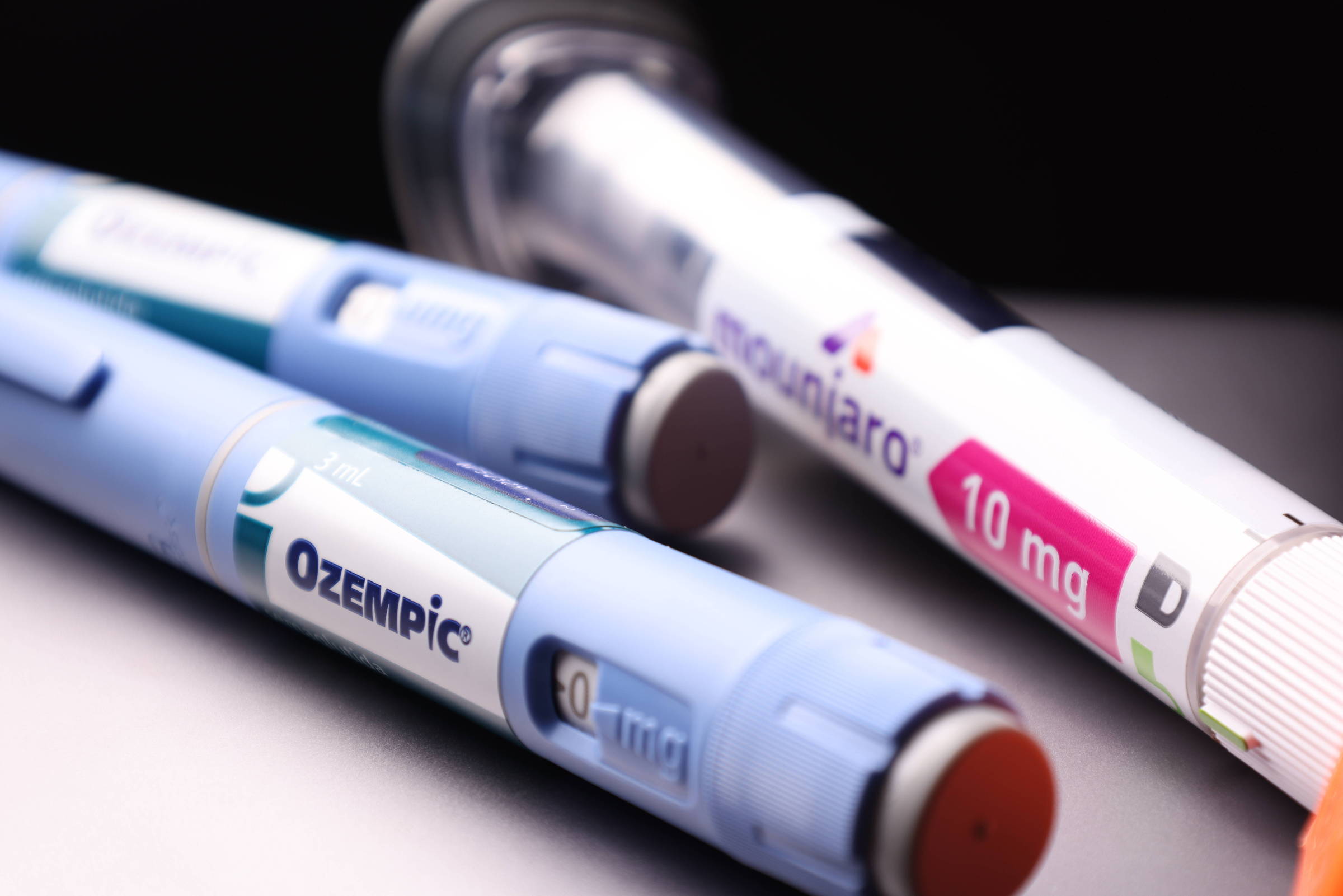 A imagem mostra duas canetas de medicamento sobre uma superfície escura. A caneta à esquerda é rotulada como