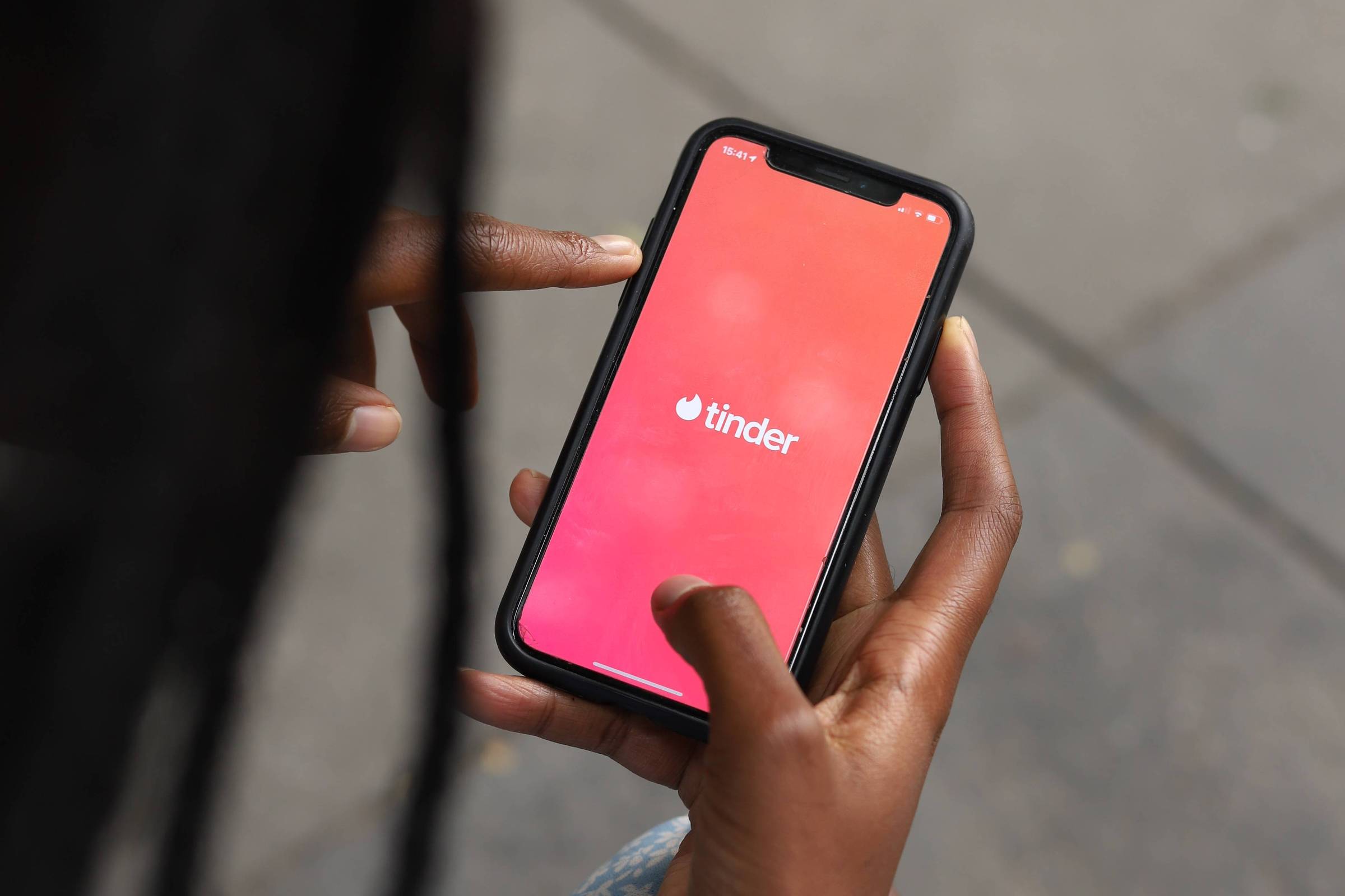 Mãos de uma mulher negra segurando um celular com a tela escrito Tinder