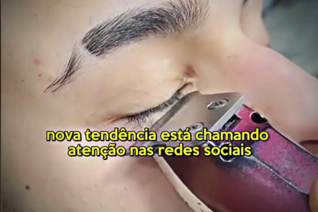 A imagem mostra um close de um rosto masculino em que uma máquina de cortar cabelo está sendo usada para aparar os cílios. O homem está com os olhos fechados e a máquina está posicionada próxima à sobrancelha. Na parte inferior da imagem, há um texto que diz: