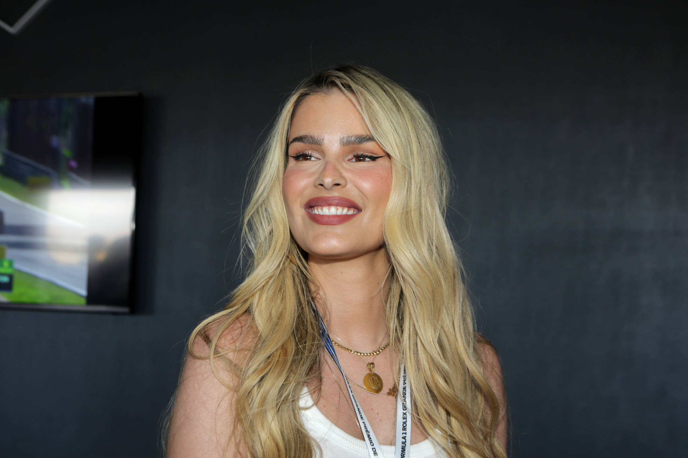 Yasmin é uma mulher branca e loira, que está sorrindo, levemente de perfil para a câmera