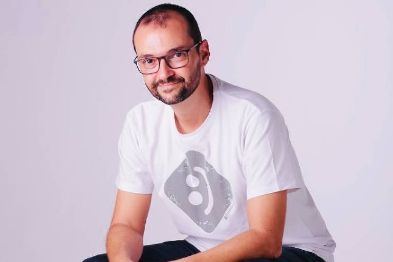 Leonardo Abrahão é um homem branco, usa óculos, e está sentado em um banco