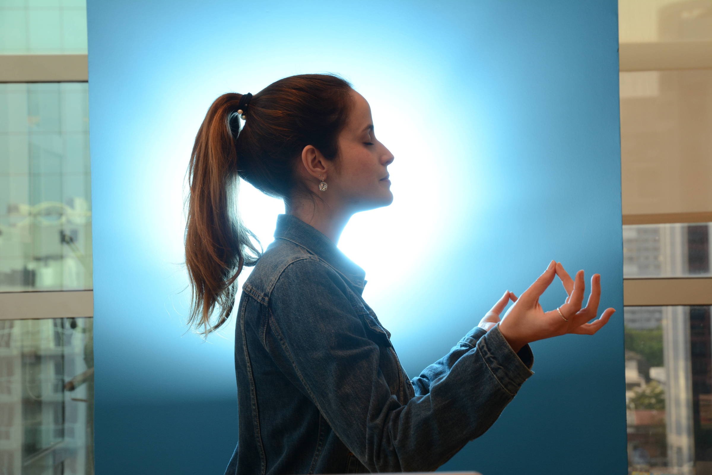 Uma mulher de cabelo preso está sentada com as mãos elevadas praticando meditação