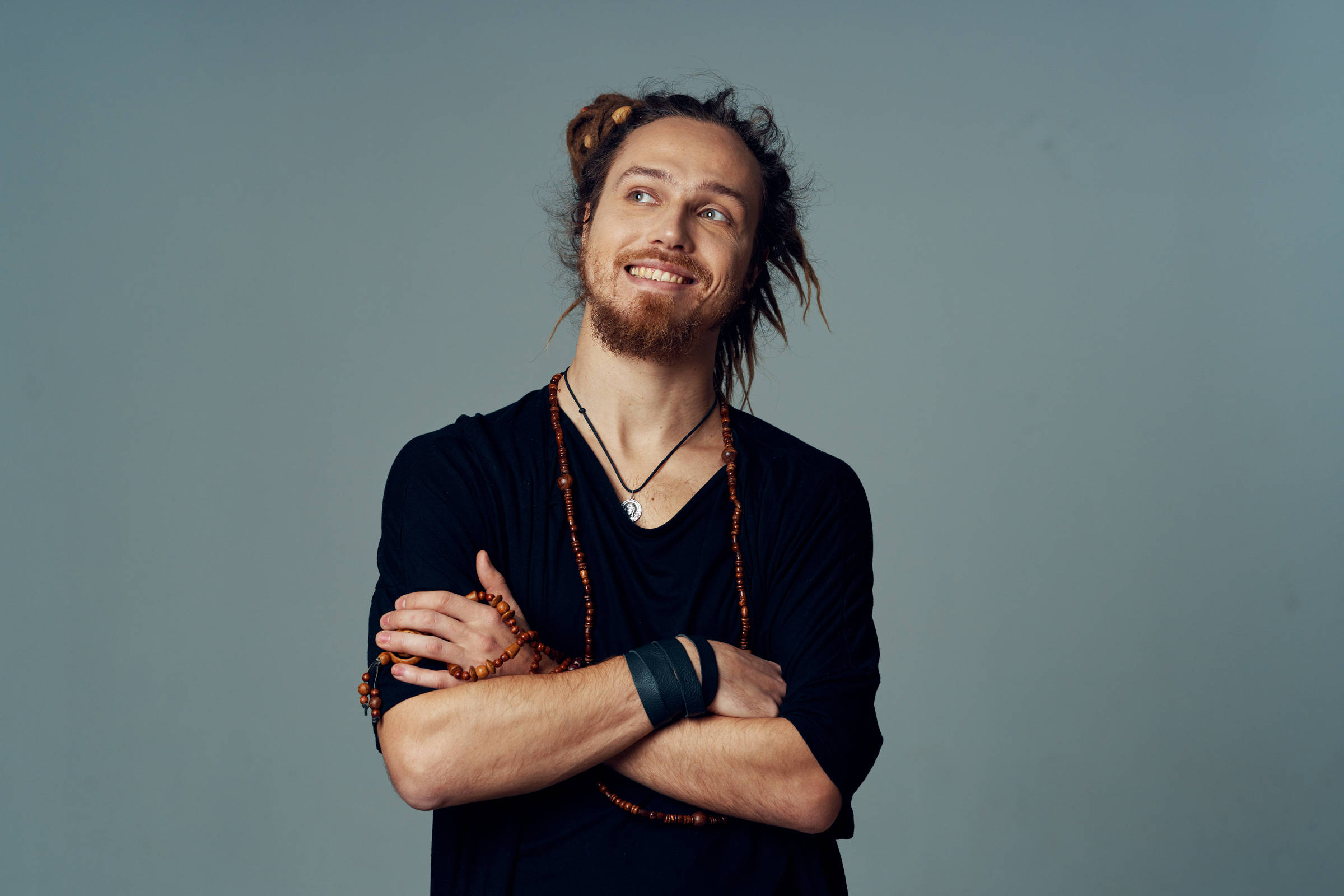 Homem jovem e branco está de braços cruzados, olhando para o alto e sorrindo