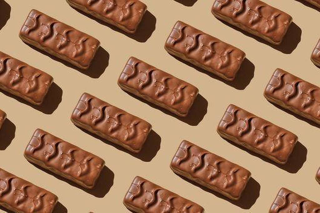 Múltiplas barras de chocolate retangulares dispostas em linhas diagonais sobre fundo bege, com sombras projetadas à direita.